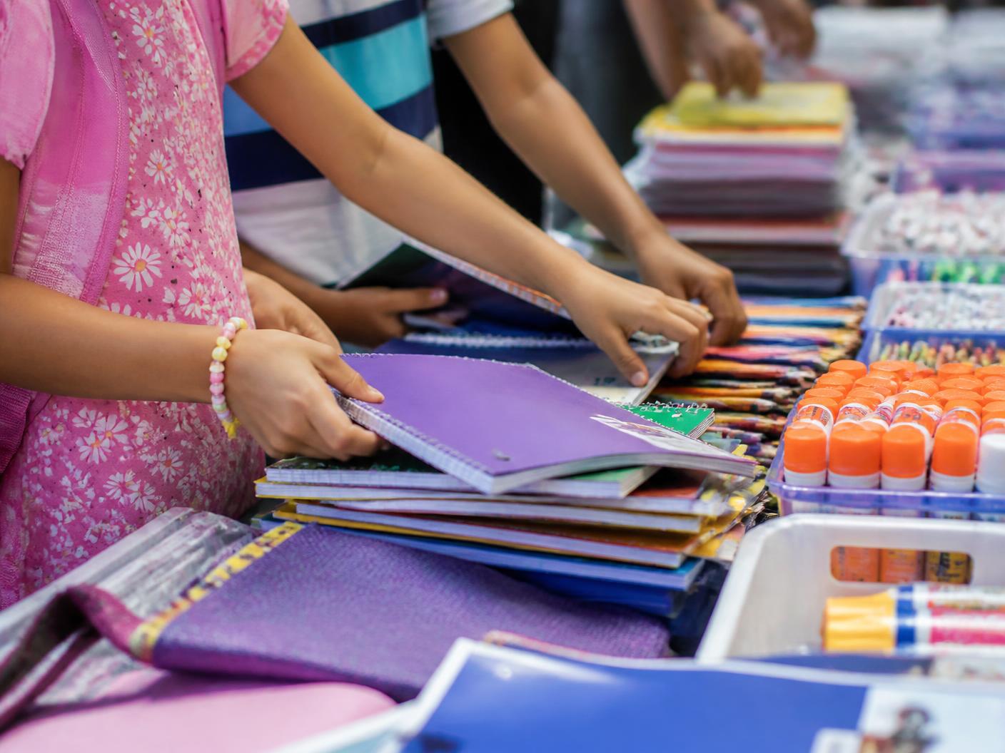 Children choose notebooks and other school supplies from a full table.